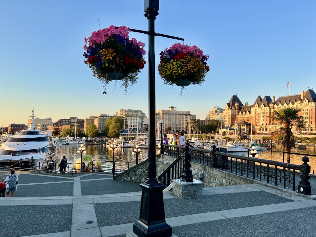 Victoria private walking tour by the Inner Harbour with hanging flower baskets, heritage buildings, and people strolling along the waterfront.